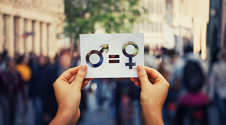  Gender equality concept as woman hands holding a white paper sheet with male and female symbol over a crowded city street background