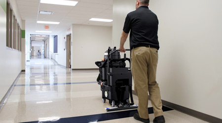 Man pushing a floor machine down an empty school hallway 