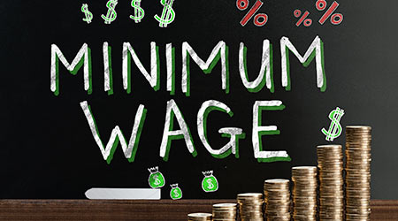 Minimum Wage At Blackboard Behind Stacked Coins