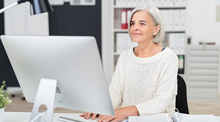 Senior businesswoman at work in the office seated at her desk typing in information on the desktop computer