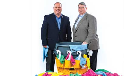 Two men in suits pose near a pile of rags