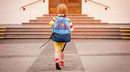 Happy smiling kid in glasses is going to school. boy with backpacking heading into an elementary school