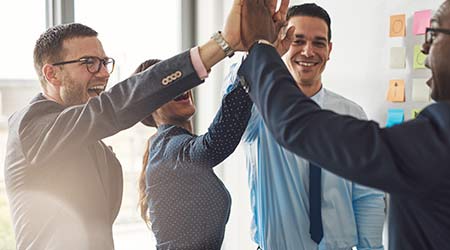 Happy successful multiracial business team giving a high fives gesture as they laugh and cheer their success