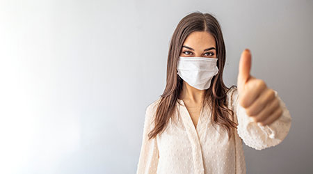  caucasian young woman with disposable face mask. Protection versus viruses and infection. Studio portrait, concept with white background. Woman showing thumb up.