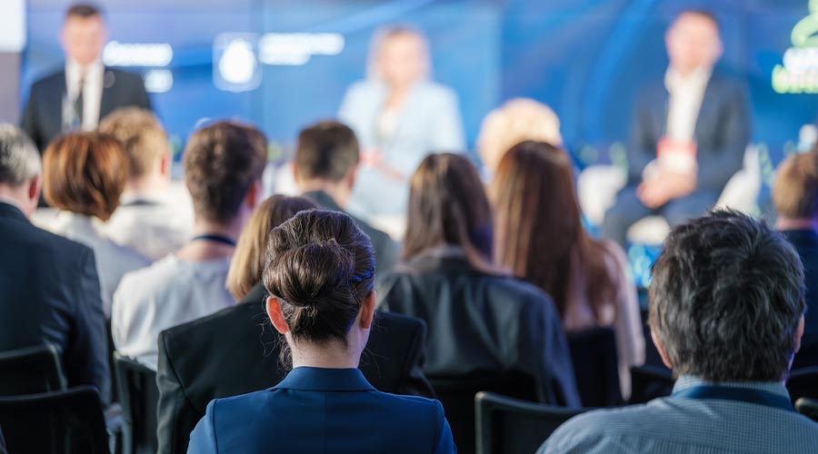 Rear view of a business audience listening to a speaker at a conference. Professional environment with engaged attendees focused on the presentation.