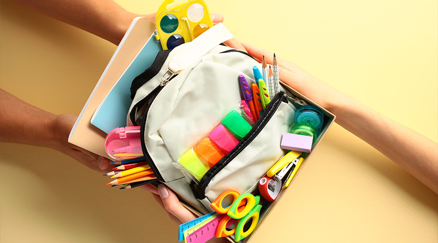 Donation box with school supplies in hands on color background. Donation, charity concept.