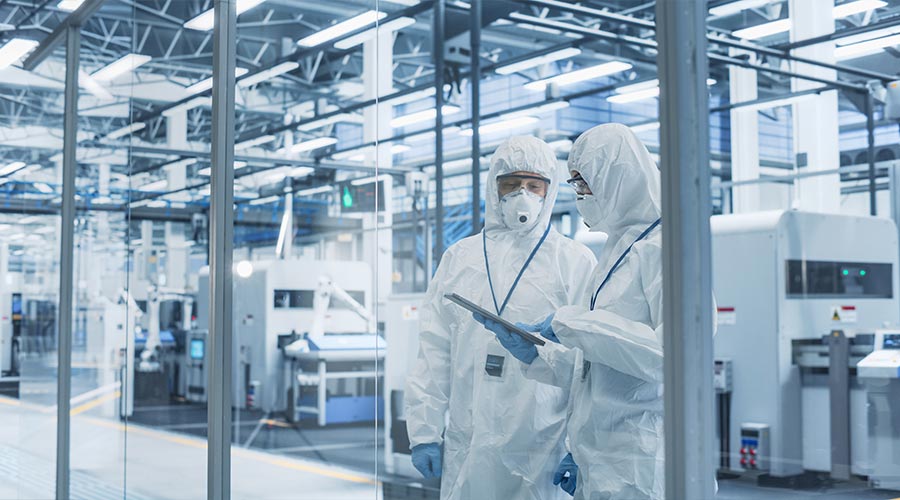 Industrial Scientists Wearing Disposable Protective Suits, Masks, and Goggles at a Production Plant. Specialist Using Tablet, Analyzing Potential Work Hazards and Contamination at a Workplac